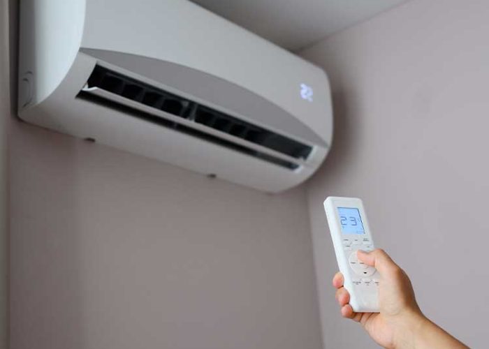Man holds remote control in front of an air conditioner, adjusting its temperature. Man sets air conditioner to comfortable temperature of 22 degrees Celsius