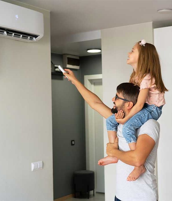 Happy family, father with little daughter on shoulders turn on air conditioner using remote control.